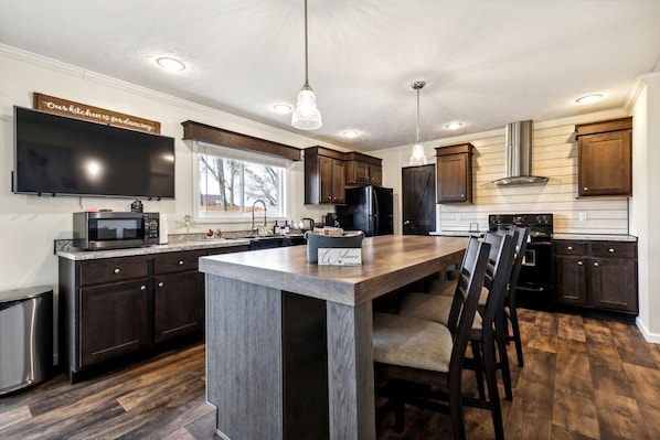 A modern kitchen with dark wood cabinets, a large island, a flat-screen TV, and a pendant light.