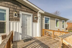 A single-story house with a front door, two windows, a wooden deck, and a mailbox.