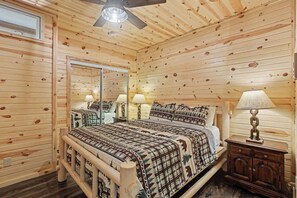 A wooden cabin room with a bed, two bedside lamps, a mirror, and a wooden cabinet.
