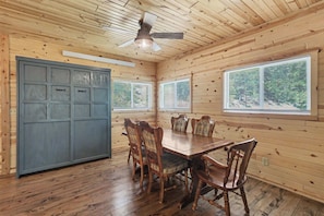 A wooden interior with a dining table, chairs, a ceiling fan, and windows.