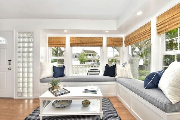 A room with a built-in bench, a white door, and a view of a house through large windows.