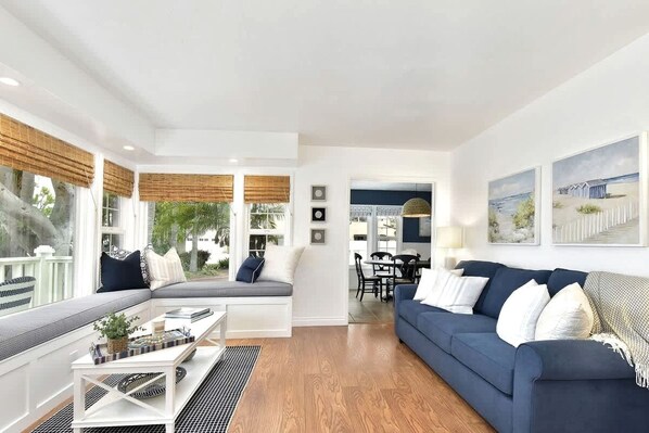 A living room with a sofa, a dining area, and a view of the outdoors.