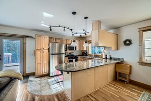 Une cuisine moderne dotée d’un îlot central, d’appareils électroménagers en acier inoxydable et d’un luminaire suspendu.