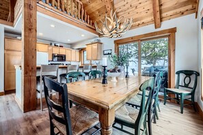 A wooden dining table with chairs, a chandelier, and a view of the outdoors.