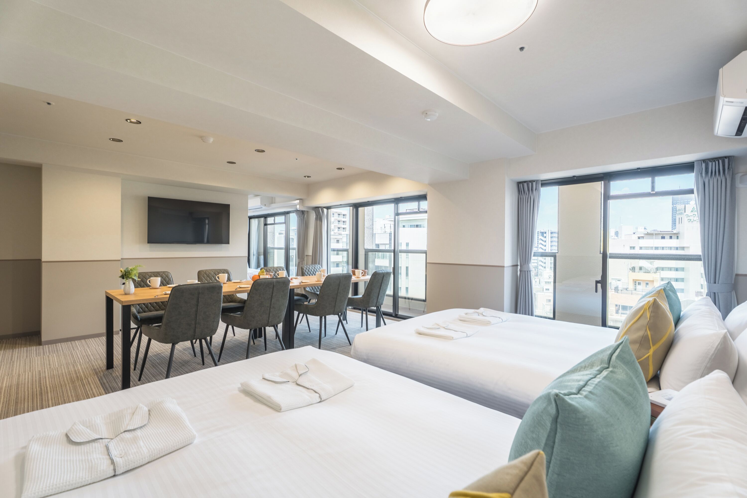 A hotel room with two beds, a dining area, and a TV mounted on the wall.