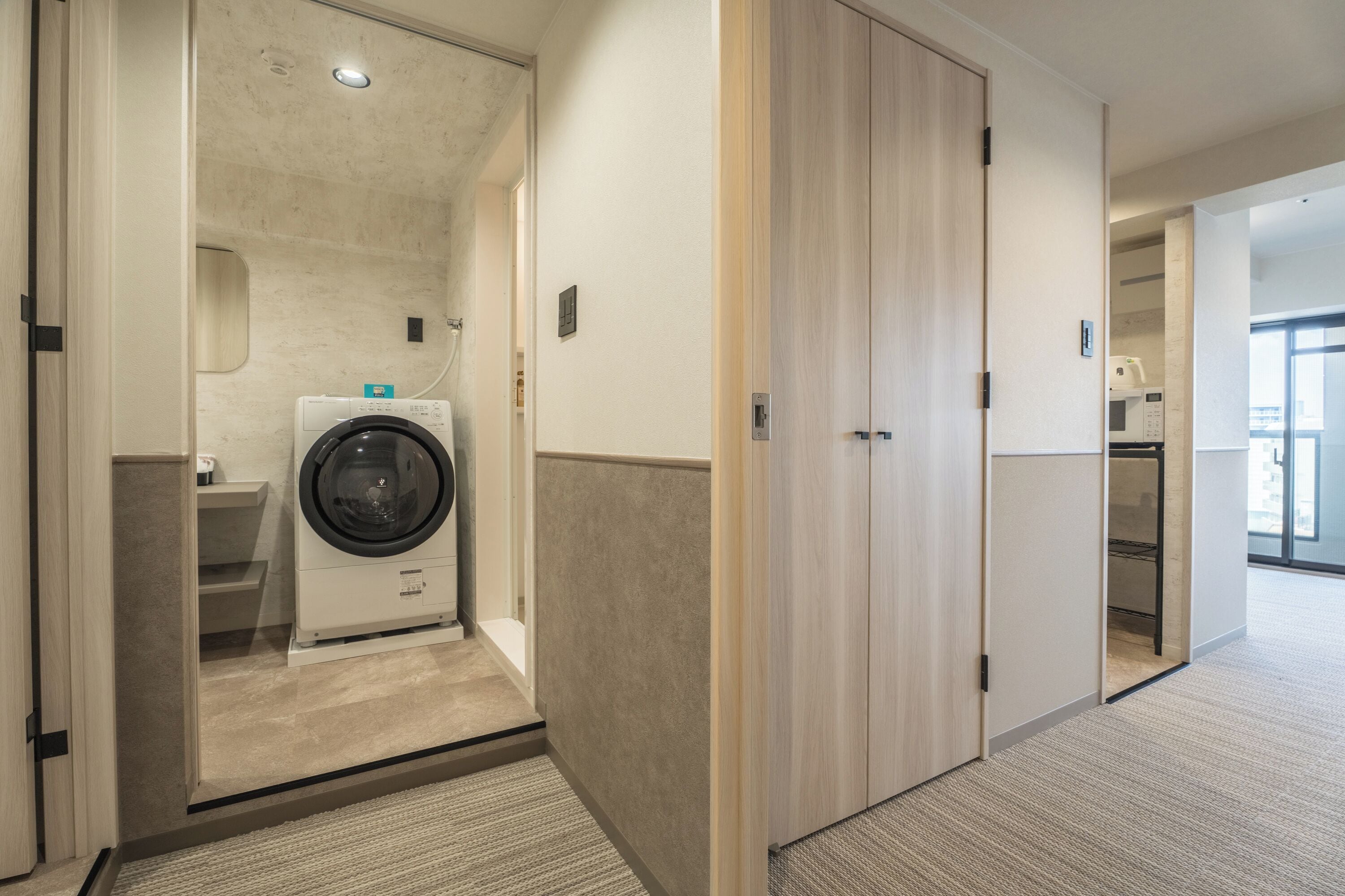 A hotel room with a washing machine, a closet, and a view of the city.