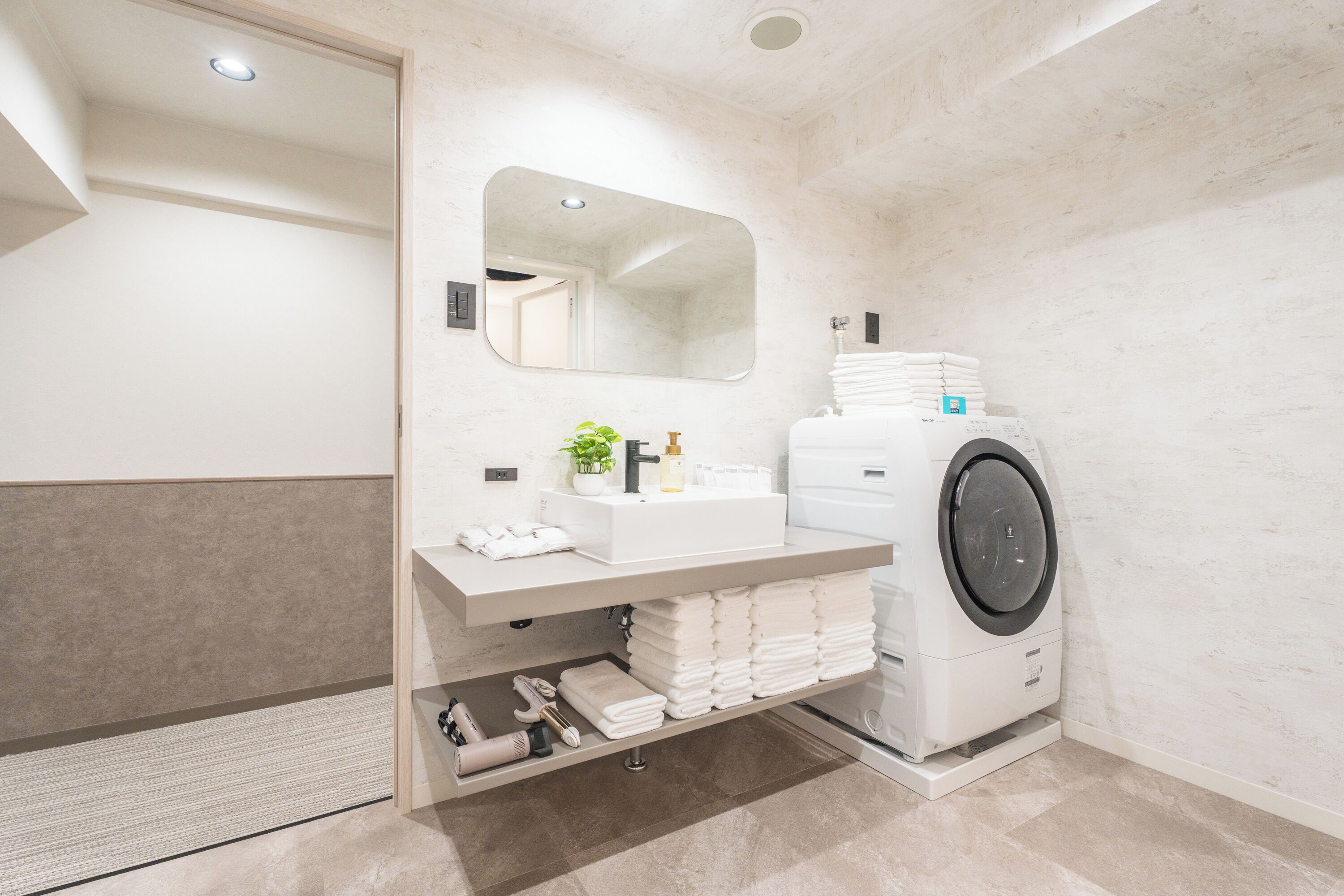 Een moderne badkamer met een ingebouwde wasmachine, een wastafel met spiegel en netjes opgevouwen handdoeken.