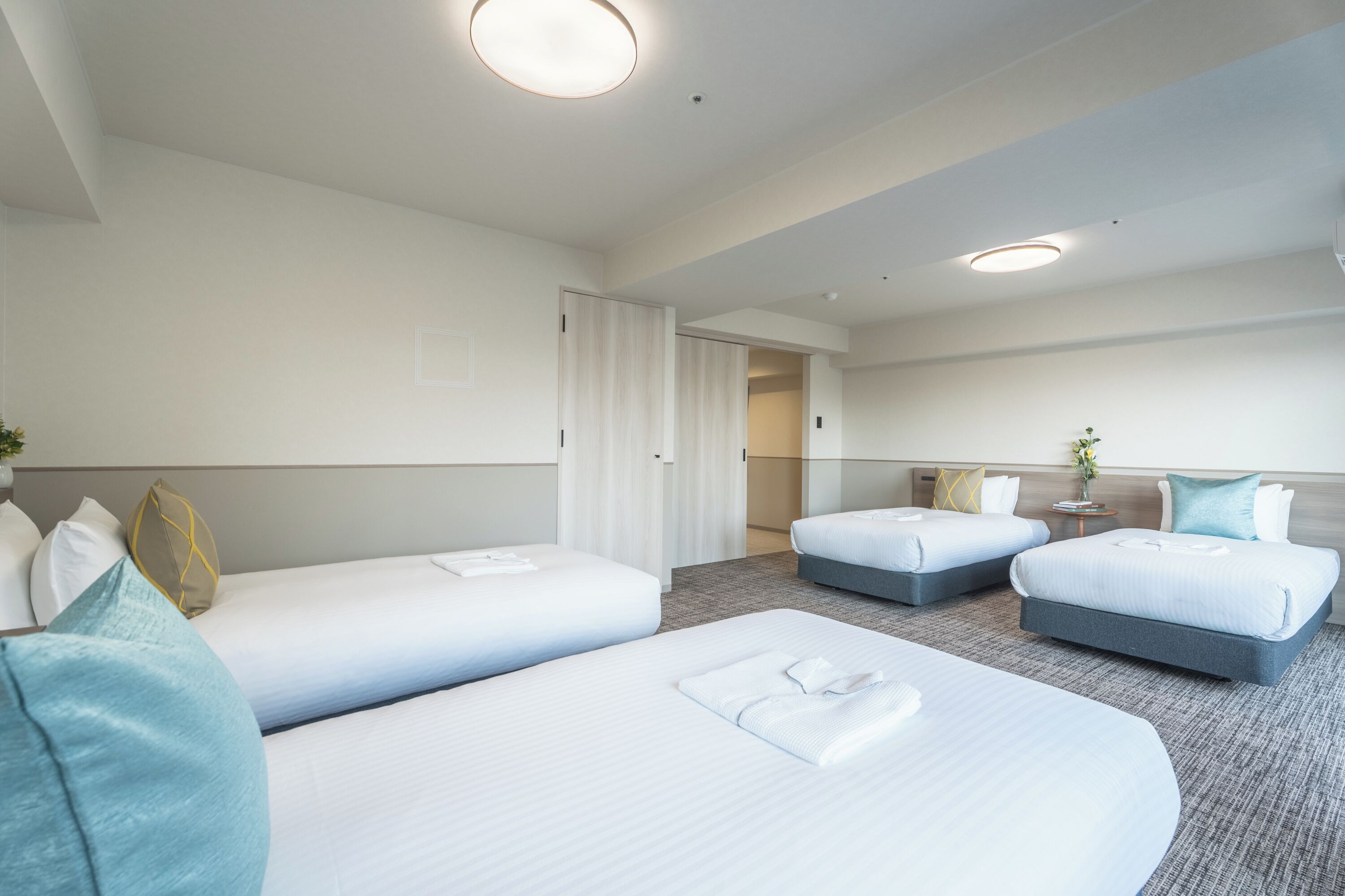 A hotel room with two single beds, a double bed, a small table, and a nightstand with a lamp.