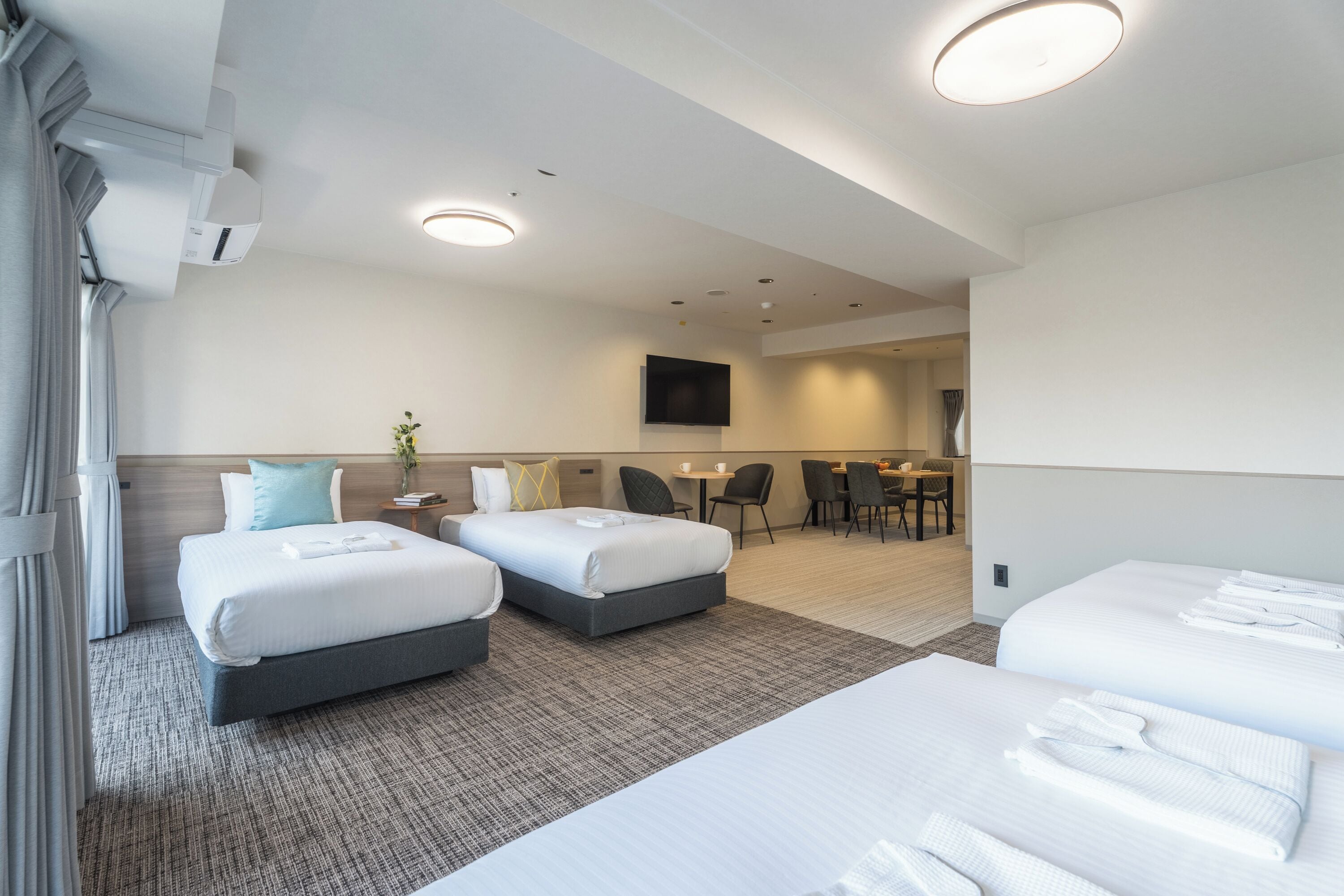 A hotel room with two beds, a flat-screen TV, a dining area, and a separate seating area.