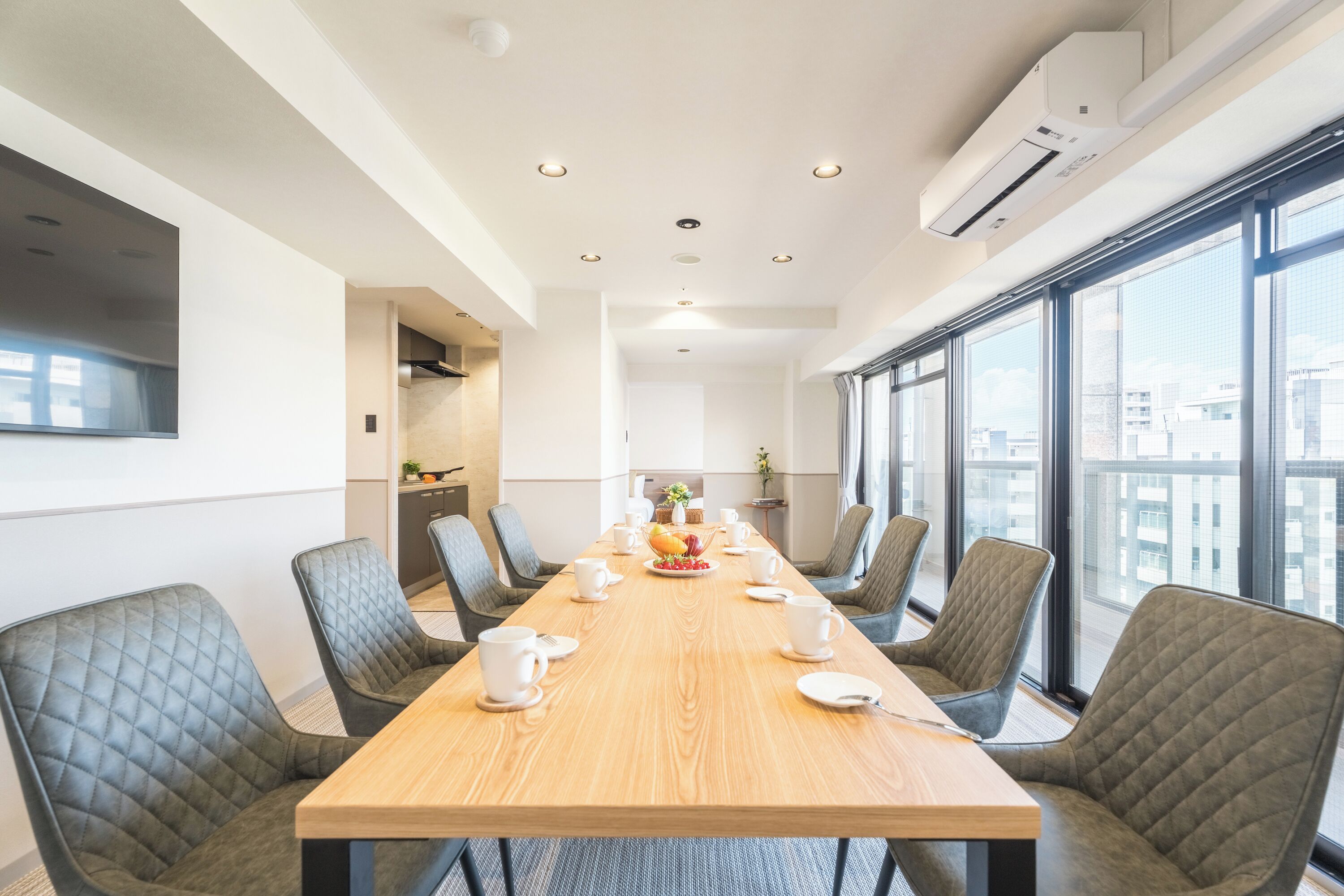 A conference room with a long table, chairs, and a view through large windows.