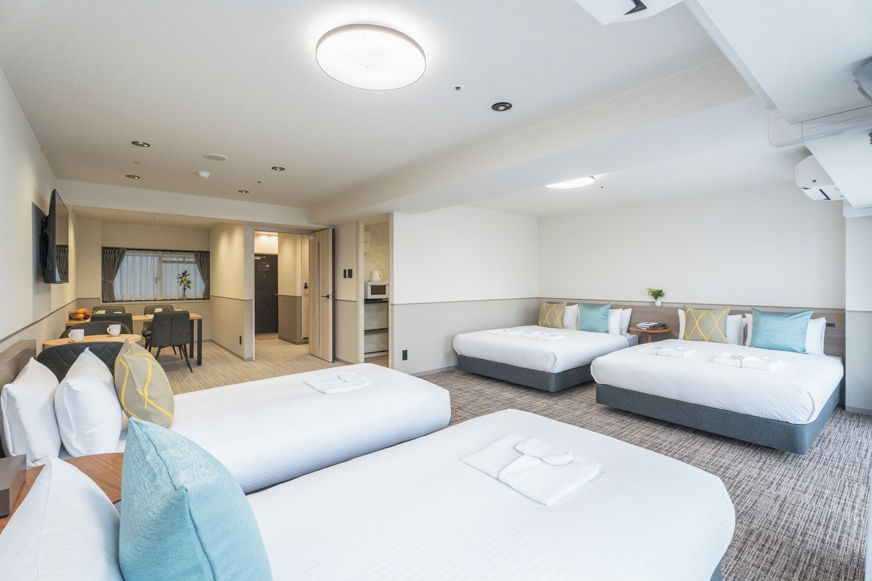 A hotel room with two beds, a desk, and a dining area.