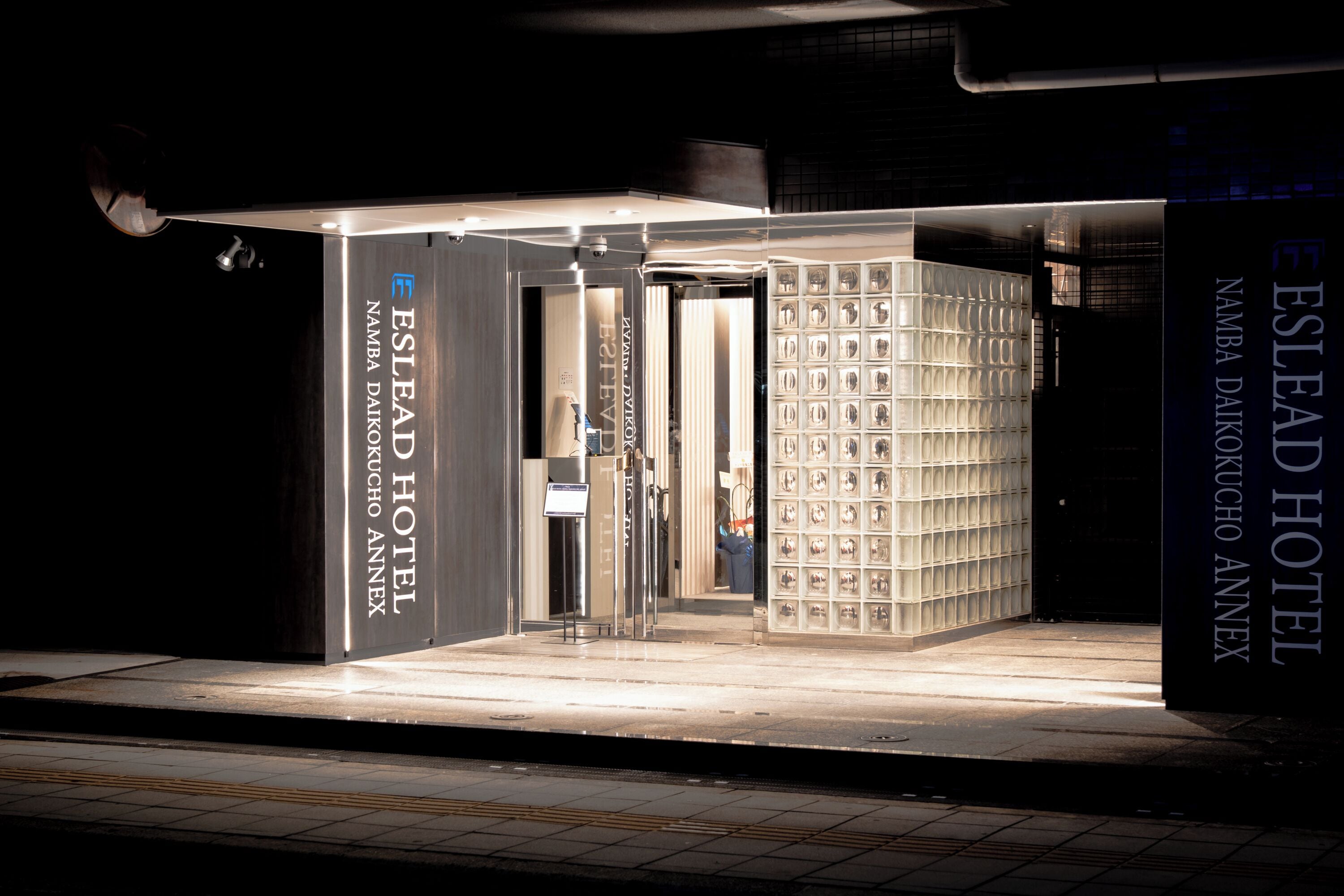 En hotelindgang med et moderne design, kendetegnet ved en metalbeklædt facade og en glasdør.