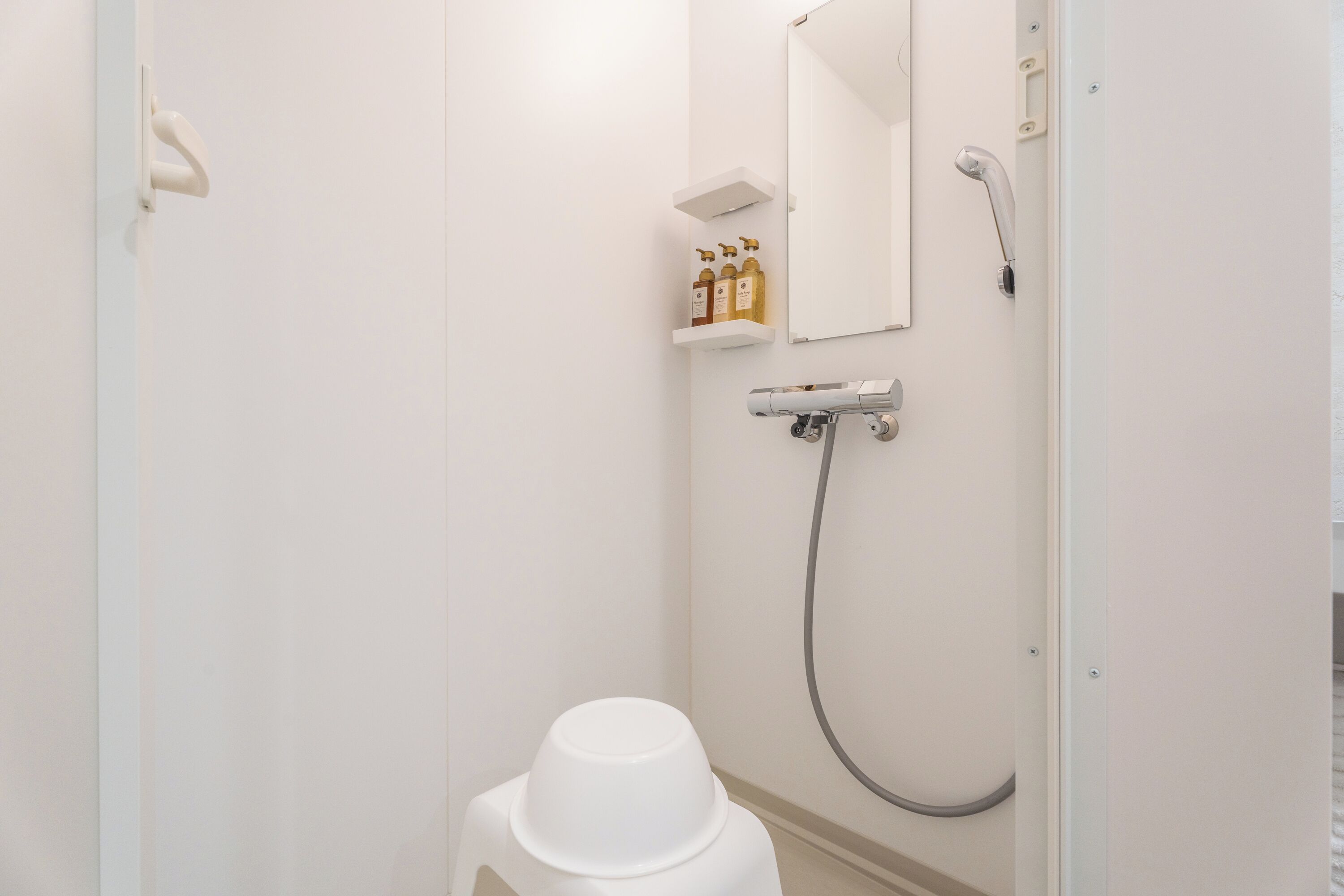 A bathroom with a toilet, a shower, a mirror, and a shelf with toiletries.