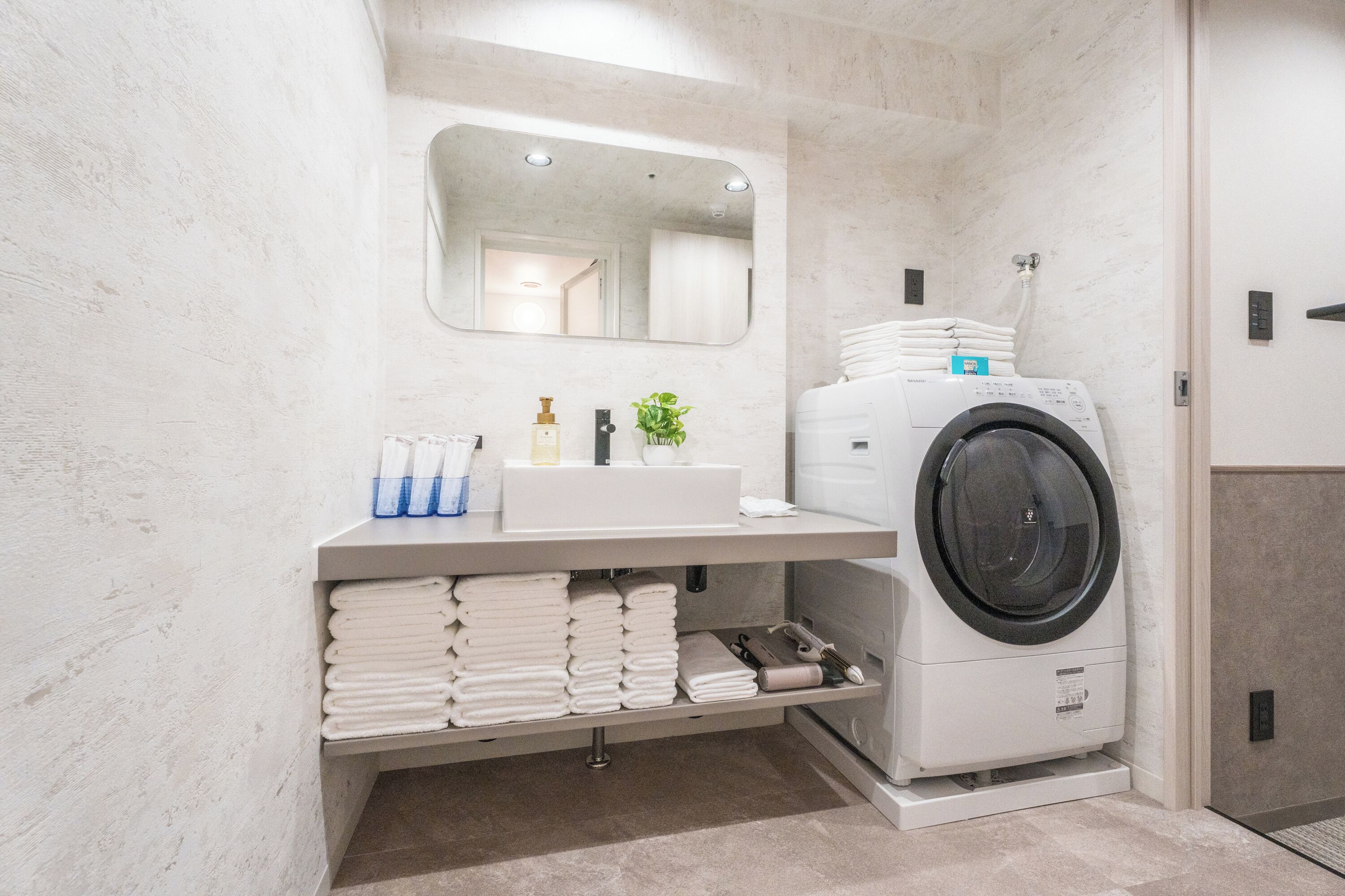 Une salle de bain moderne équipée d’un lave-linge intégré, d’un lavabo avec des articles de toilette et de serviettes soigneusement pliées.