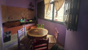 Uma cozinha com uma mesa de madeira redonda, uma cadeira, uma lixeira e uma janela com cortinas.