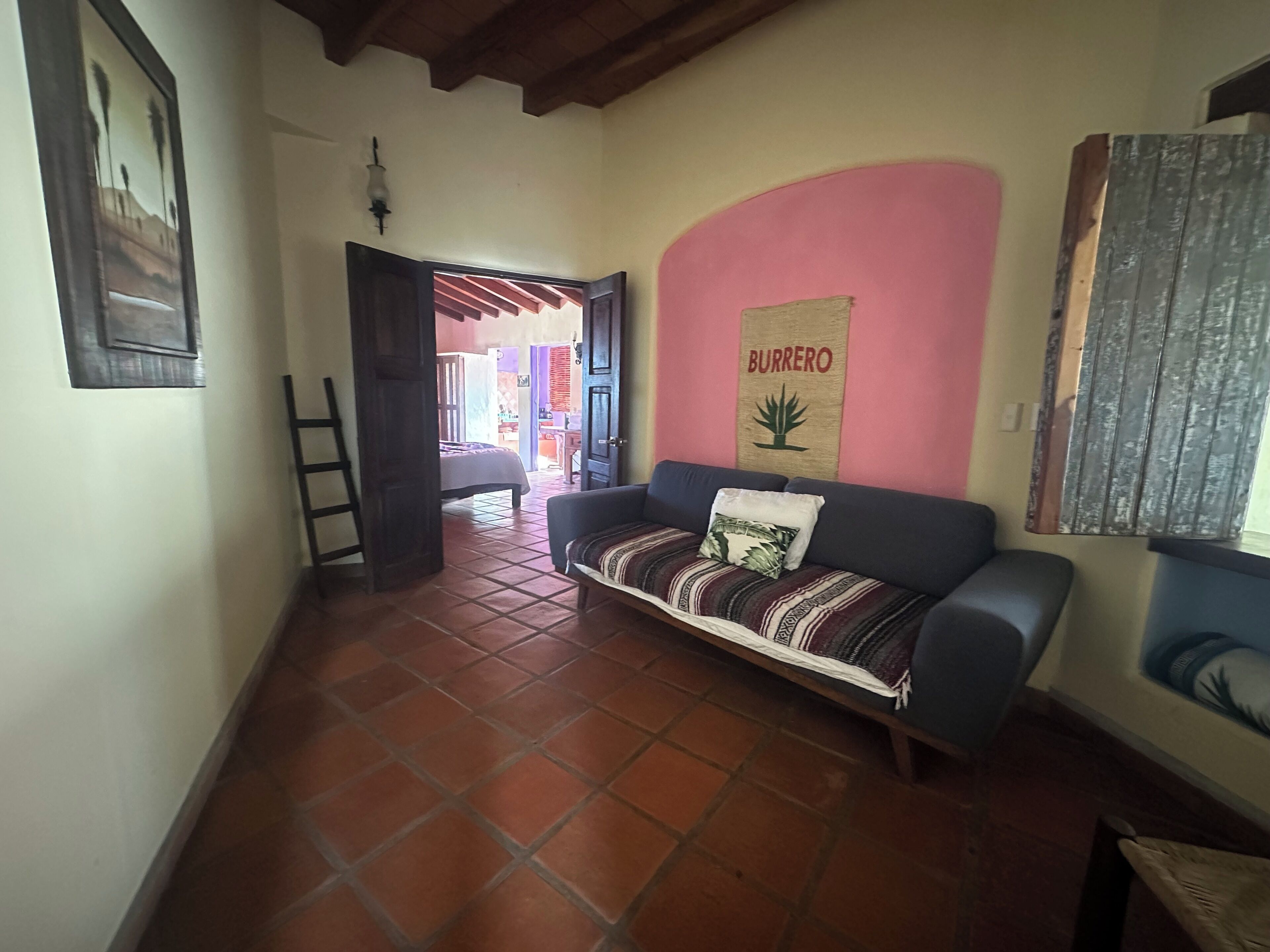 Una sala de estar con sofá, una pared con el letrero 'Burrero', una escalera y piso de baldosas.