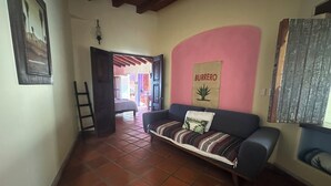 Uma sala de estar com um sofá, uma parede com o letreiro 'Burrero', uma escada e um chão ladrilhado.