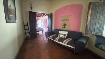 Una sala de estar con sofá, una pared con el letrero 'Burrero', una escalera y piso de baldosas.