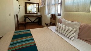 Ein Schlafzimmer mit Bett, Nachttisch, Spiegel, einem Fenster mit Vorhängen und einer Wandpflanze.
