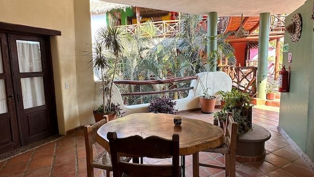 Eine Terrasse mit einem runden Holztisch und Stühlen, umgeben von Kübelpflanzen.