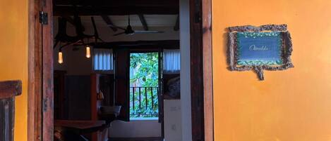 A doorway leading to a room with a stone floor, a wooden table, and a window with a view of greenery.