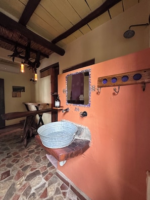 Un baño rústico con suelo de piedra, un banco de madera, un lavabo de metal y un espejo con marco decorativo.