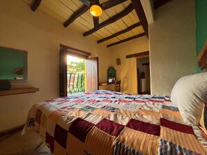 Quarto com uma cama grande, teto de madeira, janela com vista e porta para outro cômodo.