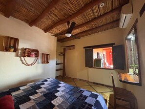 Quarto com cama, ventilador de teto, janela e porta que dá para outro espaço.