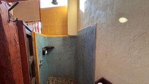 A small, narrow bathroom with a tiled floor, a shower area, and a wooden shelf with a towel. - Habitación Luisa (Segundo piso) (San Francisco)