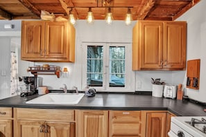 A kitchen with wooden cabinets, a black countertop, a sink, a stove, and a window with a view of trees.