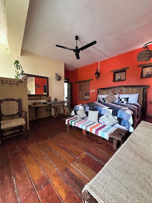 Een kamer met een bed, een plafondventilator, een houten vloer en een met baksteen beklede open haard.