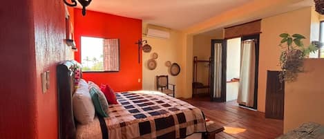 A bedroom with a bed, a wooden bench, a window, and a door leading to a balcony.
