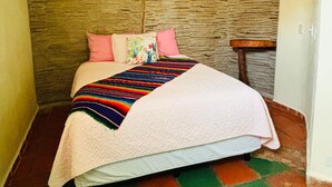 Uma cama com um cobertor colorido, almofadas cor-de-rosa e uma parede texturizada ao fundo.