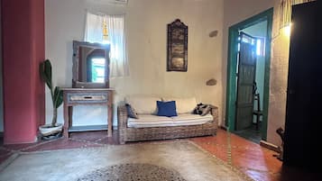 Una habitación con techo de ladrillo, un sofá con cojines, un tapete estampado, una planta en maceta y un cuadro colgado en la pared.