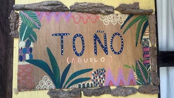 Un letrero de madera con la inscripción 'TONO (ABUELO)', rodeado de diseños coloridos y elementos naturales.