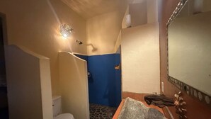 Casa de banho com sanita branca, parede azul, chão com padrão de pedra, espelho com moldura decorativa e luminária.