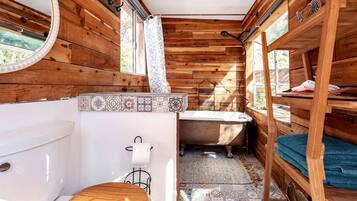 Une salle de bain rustique, aménagée dans une cabane en bois, avec des toilettes, un lavabo et une baignoire.