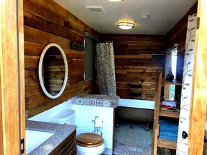 A compact bathroom with wooden walls, a toilet, a sink, and a mirror.