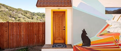 Une maison avec une porte en bois, une fresque murale colorée et une clôture en bois.