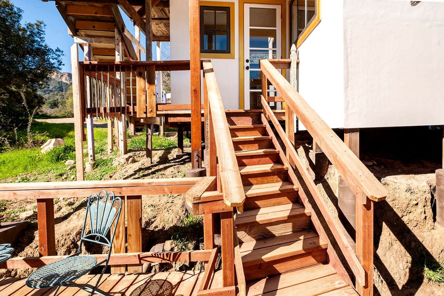 Una scala in legno conduce a un edificio con facciata bianca e una porta con pannelli di vetro.