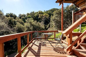 A wooden deck with a table and chairs, surrounded by a railing and overlooking a forested area.