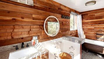 Une salle de bain avec des murs en bois, un miroir rond, une baignoire et des toilettes.