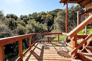 A wooden deck with a table and chairs, surrounded by a railing and overlooking a forested area.