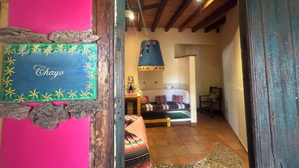 Un corridoio stretto con soffitto in legno, un letto con biancheria a motivi decorativi e una targa con su scritto 'Chayo'.