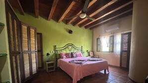 Una camera da letto con un letto, una ventola a soffitto, una finestra con tende e una porta.