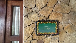 A stone wall with a plaque that reads 'Triny' and a wooden door with a window. - Habitación Triny (Primer piso) (San Francisco)