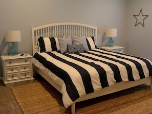 Un lit avec une couvre-lit à rayures, deux tables de chevet avec des lampes, une décoration en forme d’étoile sur le mur et un tapis tissé.