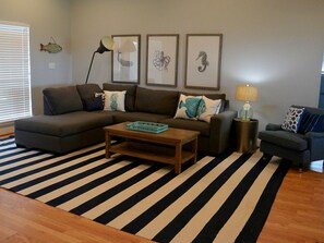 A living room with a sectional sofa, a coffee table, a side table with a lamp, and a striped rug.