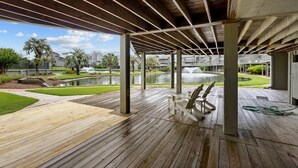 Une terrasse extérieure en bois offrant une vue sur un élément aquatique et sur des bâtiments en arrière-plan.
