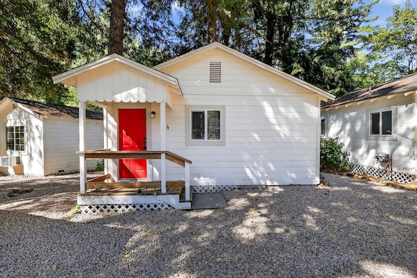 A small white cabin with a red door, a porch, and a window.